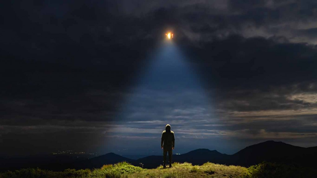 The UFO shines on a male standing on the mountain