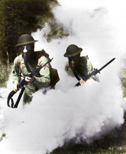 Two U.S. soldiers wear gas masks while walking through plumes of smoke.