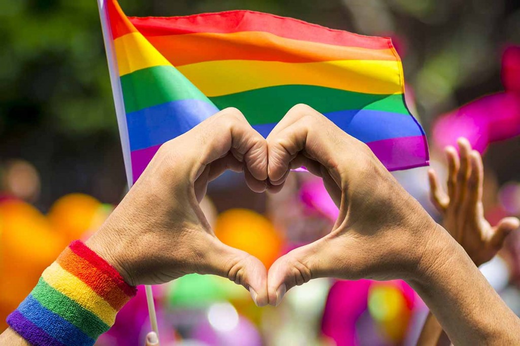 Supporting hands make heart sign and wave in front of a rainbow