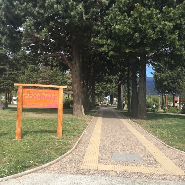 Uno de los accesos peatonales de la Plaza de Armas de Cochrane, rodeada de numerosos pinos.